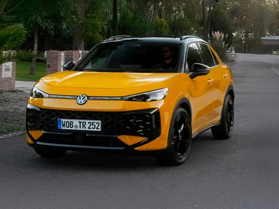 Frontansicht eines Volkswagen T-Roc Life in moderner SUV-Optik mit markantem Kühlergrill, schmalen LED-Scheinwerfern und erhöhtem Fahrwerk, aufgenommen bei Tageslicht auf einer Straße.