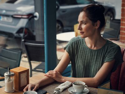 Eine BMW Kundin trinkt entspannt ihren Kaffee, während ihr Fahrzeug in der Werkstatt des Servicepartners gewartet wird.