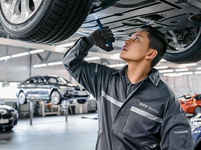 Kfz-Mechatroniker unter einem BMW welcher mit einer Taschenlampe den Reifen begutachtet