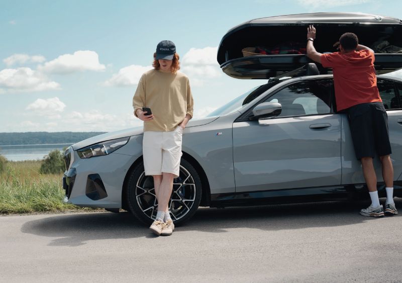 BMW 5er Touring mit Dachgepäckträger un dzwei Personen am Auto stehend auf einer Landstrecke